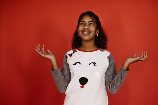 A Smiling Girl Wearing Braces Standing Against a Red Background and Holding Both Hands Up
